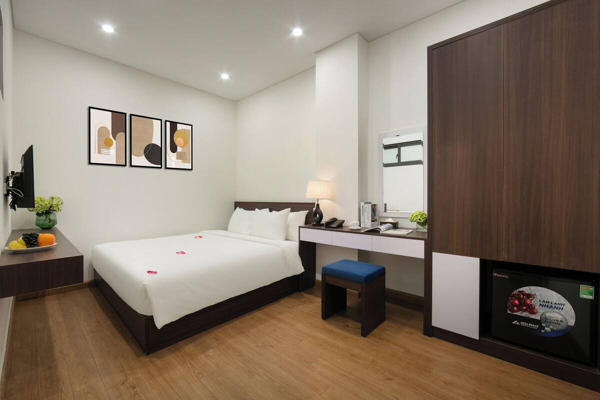 A hotel room with a bed, bedside table, desk, chair, and a TV.