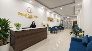 A hotel reception area with a reception desk, a woman behind it, and a seating area with tables and chairs. - Queen Cafe Hotel (Hanoi)
