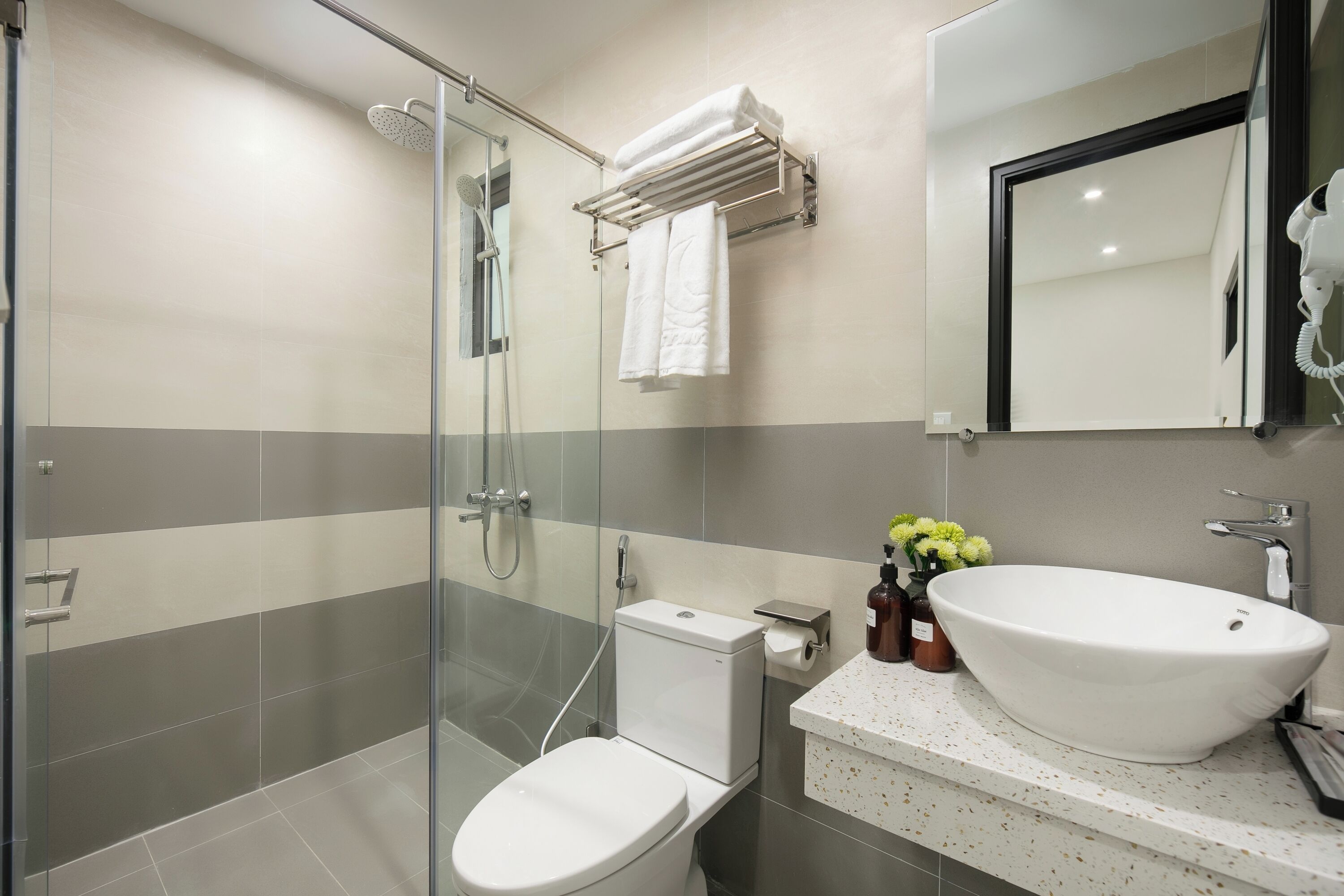 A modern bathroom with a glass-enclosed shower, a white toilet, a large white sink, and a mirror above the sink.