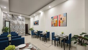 A modern dining area with blue chairs, marble tables, and potted plants. - Queen Cafe Hotel (Hanoi)