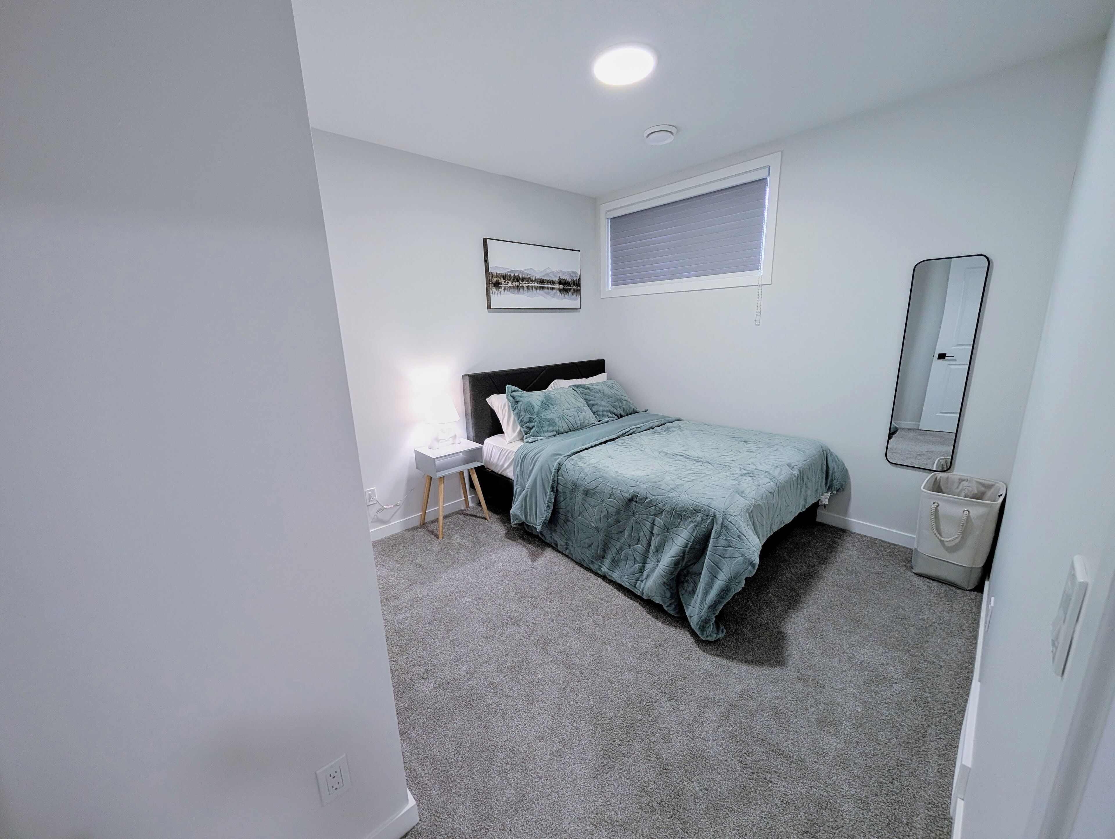 Un dormitorio con cama, mesita de noche, lámpara, ventana y espejo.