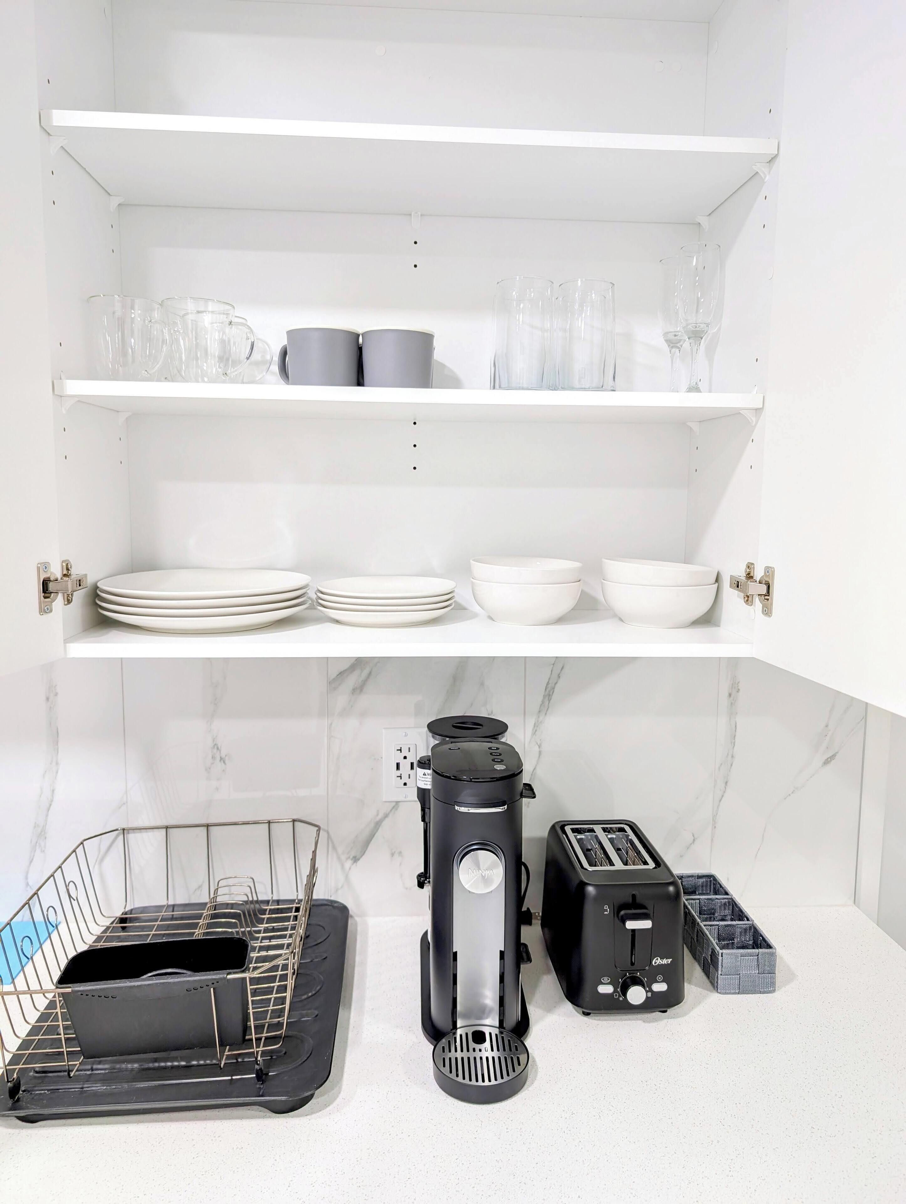Una cucina con ripiani bianchi, una macchina da caffè, un tostapane e un espositore per piatti.