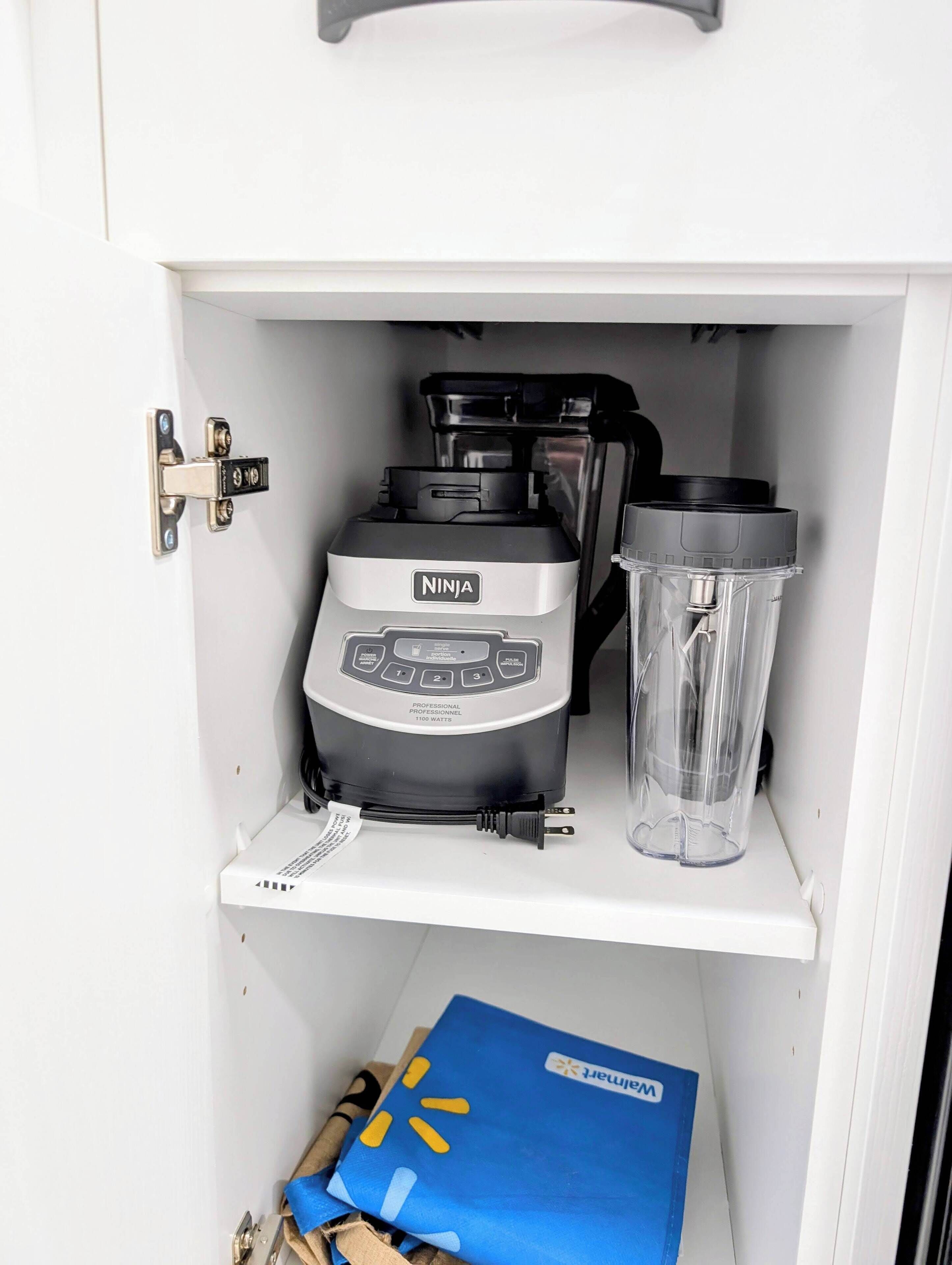 A white cabinet with a Ninja Professional blender and a clear container on the shelf.