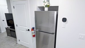 A modern kitchen with a stainless steel refrigerator, a white door, and a small cabinet with a television. - Cozy 2BR Suite | Near CTrain, Spruce Meadows & Parks | Modern Comforts Await! (Calgary)