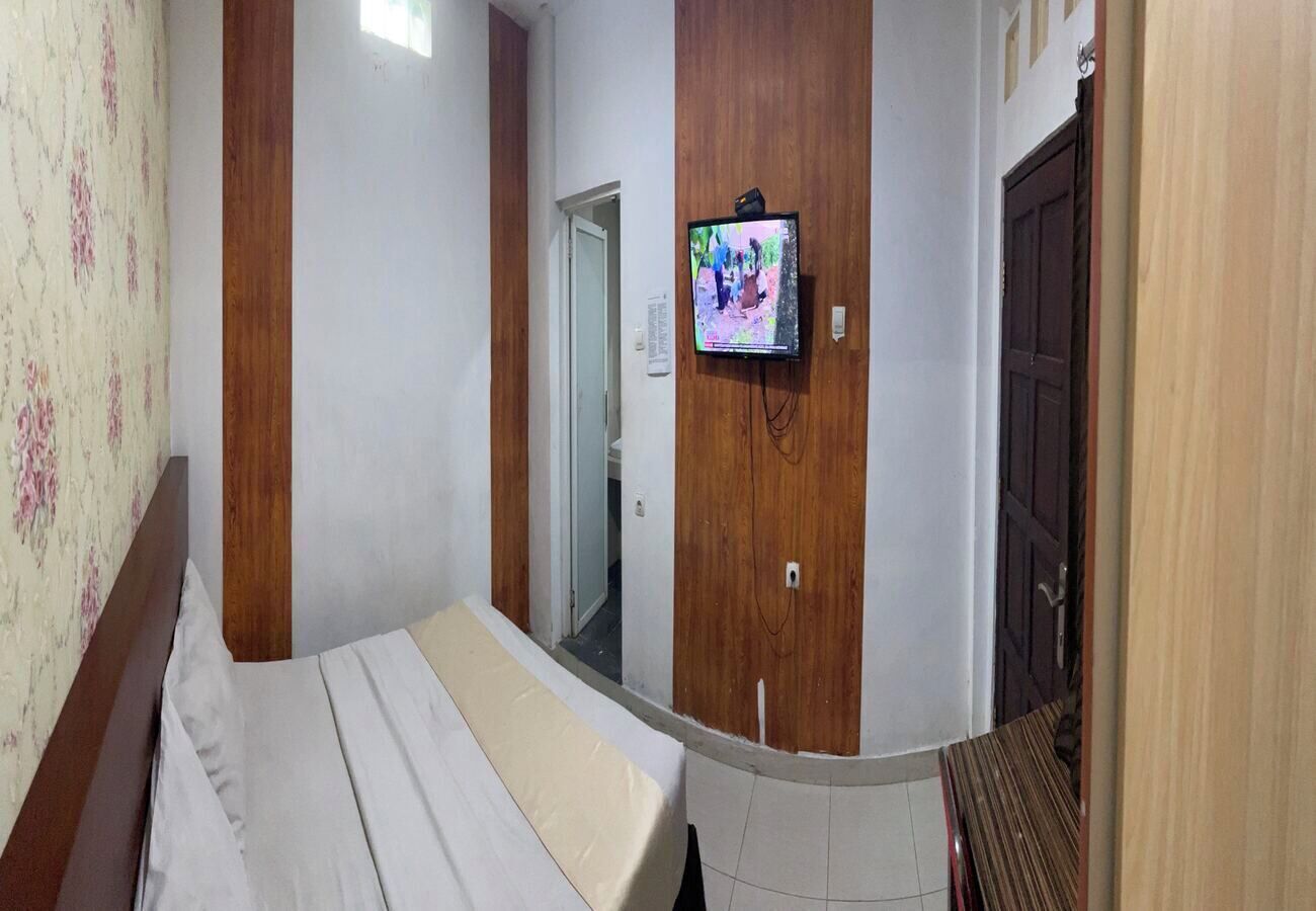Une chambre à coucher avec un lit, des murs recouverts de panneaux en bois, un téléviseur fixé au mur et une porte donnant sur une autre pièce.