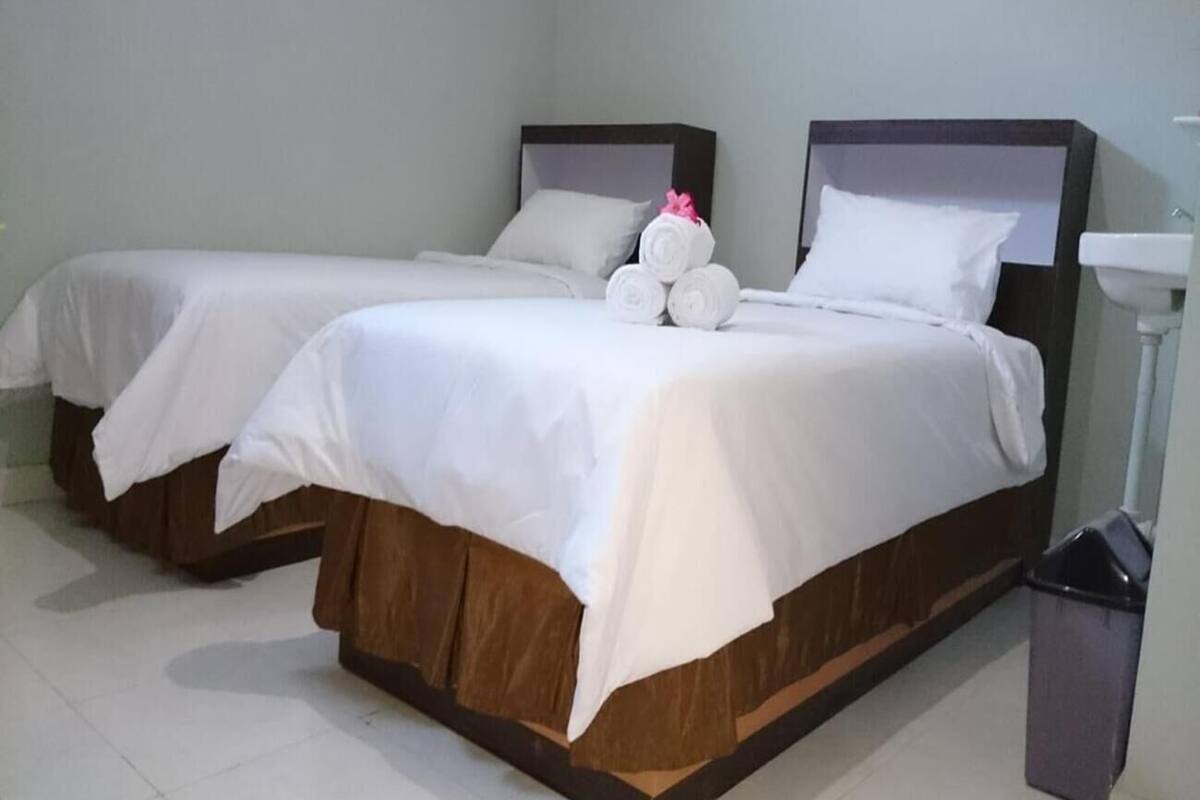 Ein Hotelzimmer mit zwei Einzelbetten, einem weißen Waschbecken und einem Mülleimer.