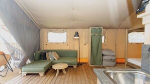 L’intérieur d’un chalet accueillant, avec un canapé vert, une petite table ronde, une lampe, un lit superposé et un évier.