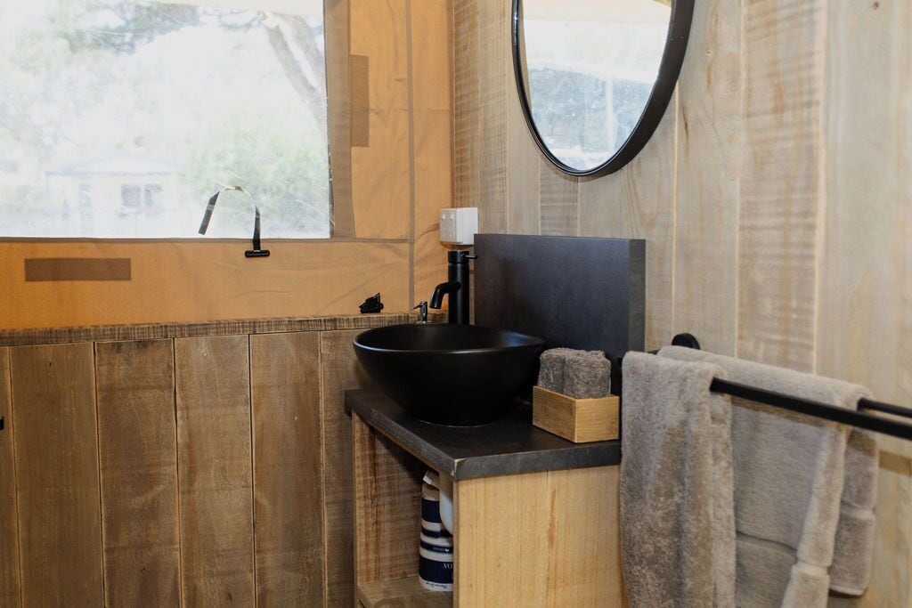 A bathroom with a wooden vanity, a black sink, a mirror, and a towel rack.