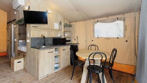 Une cuisine compacte équipée d’un four à micro-ondes encastré, d’un évier et d’étagères. On y trouve une table à manger avec quatre chaises et une fenêtre avec des rideaux.