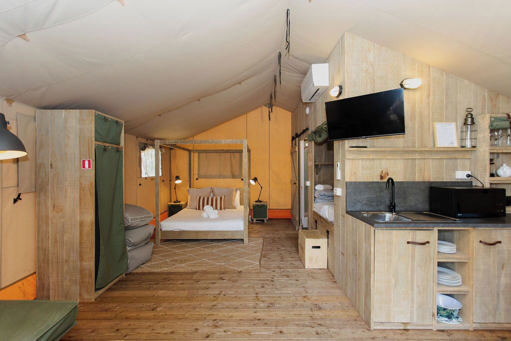 Una habitación compacta y bien iluminada con una cama, un pequeño kitchenette y un televisor.