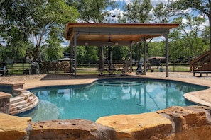 Une piscine agrémentée d’une pergola, d’un escalier en pierre et d’un espace clos avec des sièges d’extérieur.