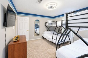 A room with bunk beds, a wooden dresser, a flat-screen TV, and a door.