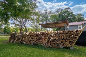 A stack of firewood in a grassy area with a house in the background.