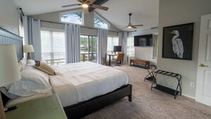 A bedroom with a large bed, ceiling fans, a desk, a chair, a bench, and a mounted TV. - Pool, Spa, Bar + Game Room - Huntsville Lake House (Huntsville)