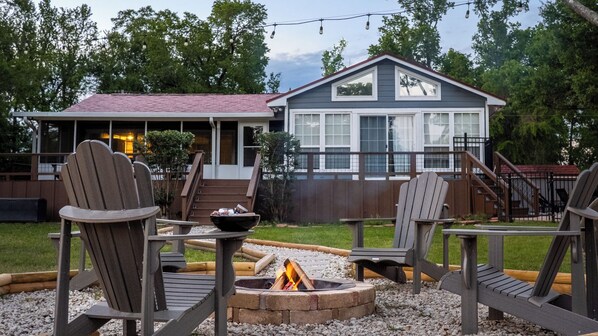 A house with a deck, a fire pit, and Adirondack chairs.