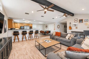 A spacious living area with a sofa, coffee table, and chairs, a dining area with a table and chairs, and a kitchen with wooden cabinets and appliances. - Pool, Spa, Bar + Game Room - Huntsville Lake House (Huntsville)