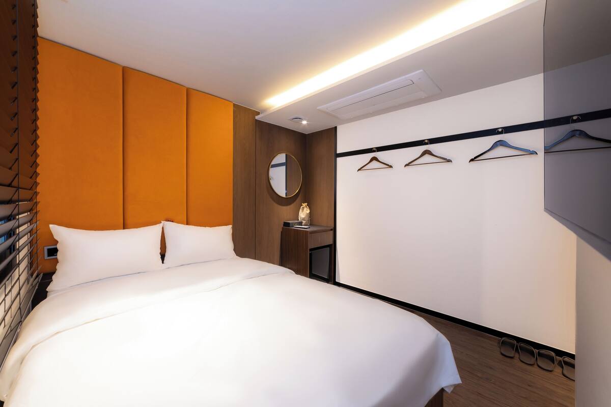 A hotel room with a large bed, a bedside table, a mirror, and a wall-mounted coat rack with hangers.