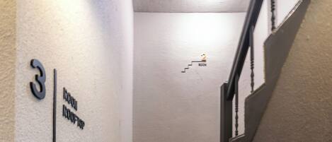Una escalera con barandilla y una pared con números y nombres de habitaciones.