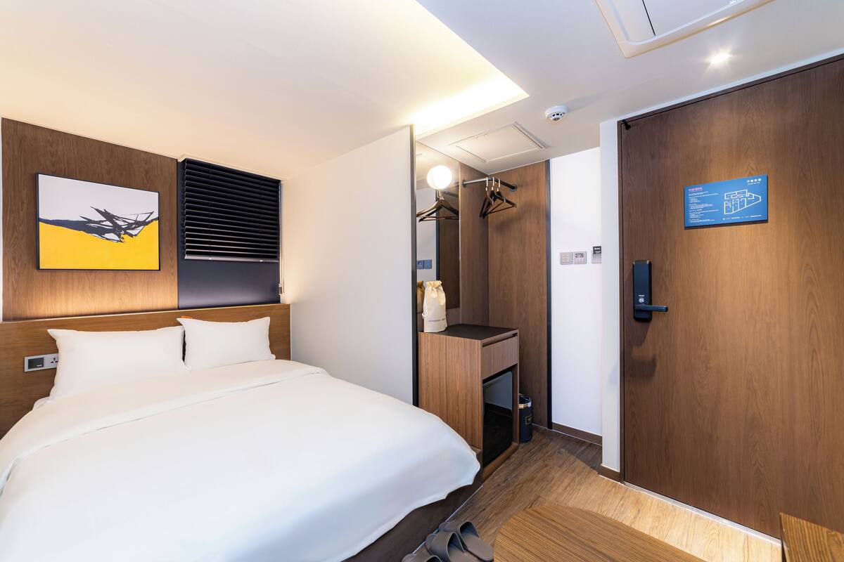 A hotel room with a bed, a mirror, a wardrobe, and a wall-mounted artwork.