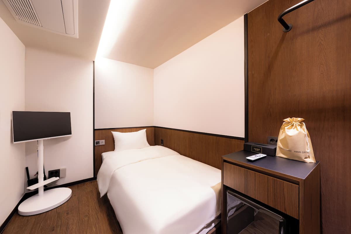 A hotel room with a bed, a flat-screen TV, a hair dryer, and a minibar.