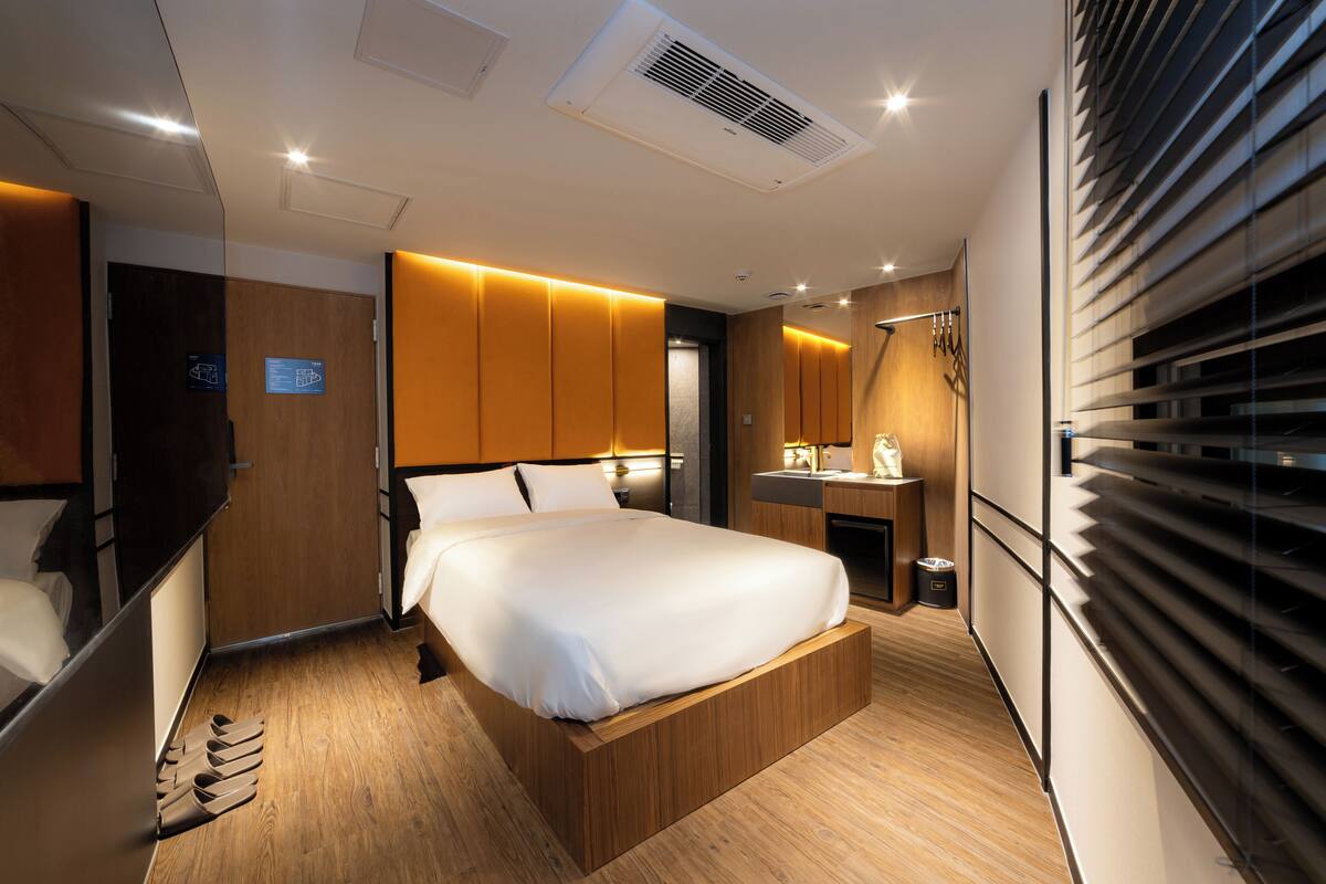 A modern hotel room with a wooden bed, built-in wardrobe, and a small bathroom.