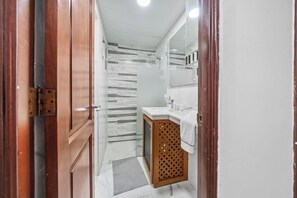 A bathroom with a shower, a vanity with a mirror, and a wooden cabinet. - Cozy 2-bedroom Apartment in Santo Domingo's Heart (Santo Domingo)