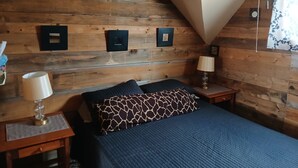 A bedroom with a sloped ceiling, wooden panel walls, a bed with a blue quilt, two bedside tables with lamps, and framed pictures on the wall. - Snowmobile, UTV trails, Fishing in a charming 3-bedroom house in Republic (Republic)