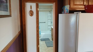 A kitchen with a white refrigerator, wooden cabinets, and a door leading to a bathroom with a bathtub and a shower. - Snowmobile, UTV trails, Fishing in a charming 3-bedroom house in Republic (Republic)