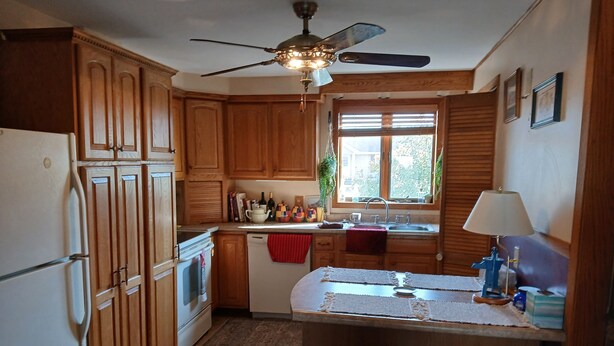 A kitchen with wooden cabinets, a ceiling fan, a window with blinds, a sink, and a small island with stools. - Snowmobile, UTV trails, Fishing in a charming 3-bedroom house in Republic (Republic)