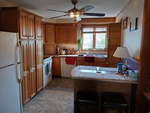 Eine Küche mit Holzausstattung, Deckenventilator, Fenster mit Jalousien, Spüle und einer kleinen Kücheninsel mit Hockern.
