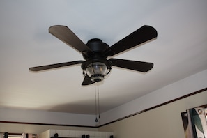 Un ventilador de techo con cuatro aspas y una lámpara central en una habitación con paredes blancas y molduras de madera.
