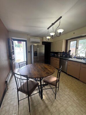 A kitchen with a round wooden table, two chairs, a refrigerator, a sink, and cabinets.