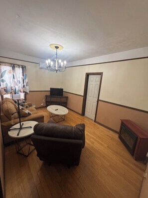 A living room with a brown leather sofa, a small round table, a TV, and a chandelier.