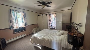 Une chambre à coucher avec un lit, un ventilateur de plafond, un radiateur et une fenêtre avec des rideaux.