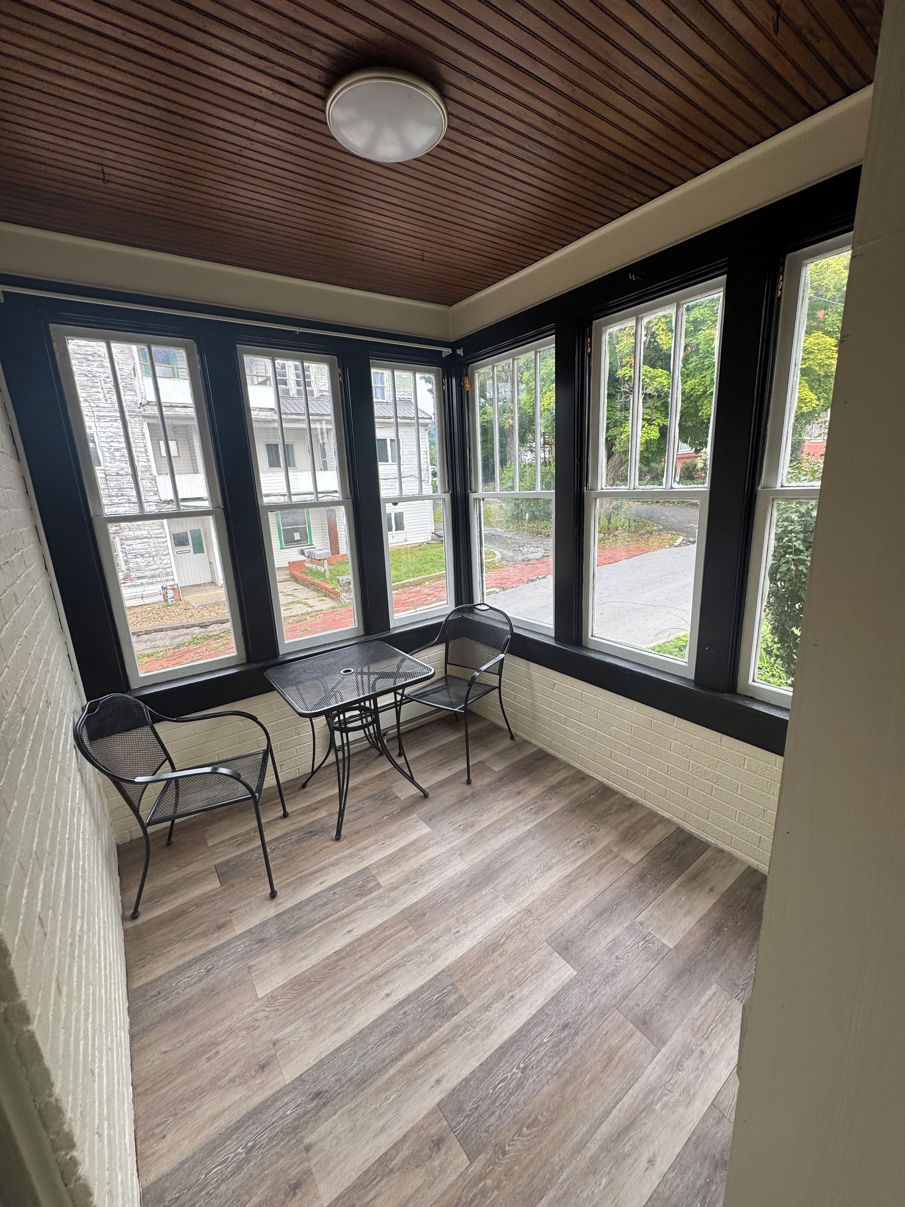 Una habitación con techo de madera, ventanas amplias, una mesa con sillas y una pared de ladrillo.