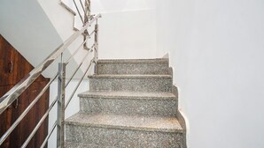 A staircase with granite steps and metal railings, leading to a landing with a wooden door and a wall-mounted light fixture. - Fabhotel The Pleasure Stay (Varanasi)