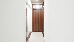 A hallway with a wooden door, white walls, and a tiled floor. - Fabhotel The Pleasure Stay (Varanasi)