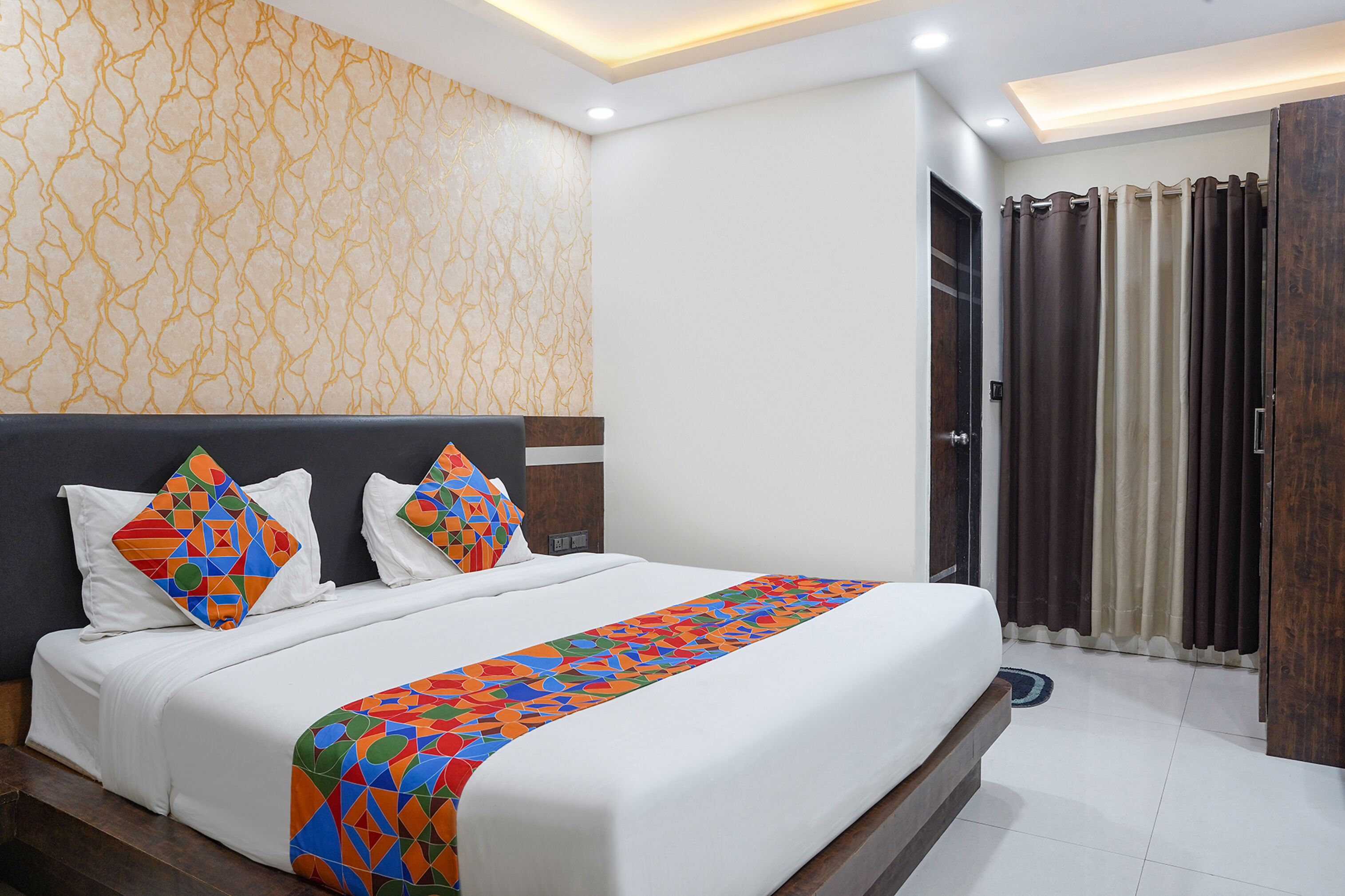A neatly made bed with a colorful geometric-patterned throw, a dark headboard, and a patterned wall.