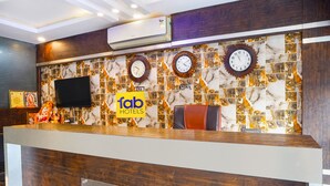 Een receptie met een marmeren muur, klokken, een televisie en een bord met 'fab hotels'.