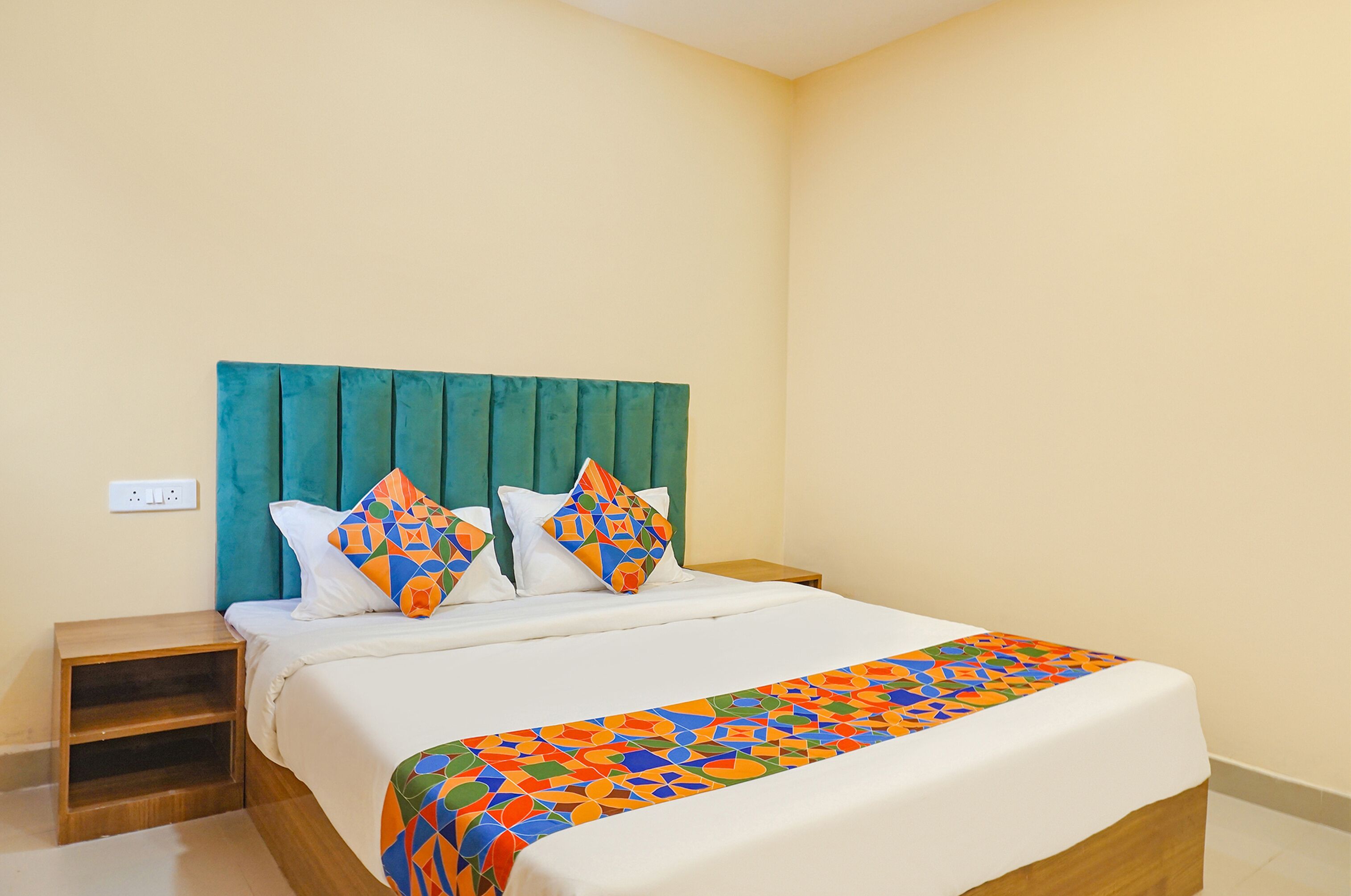 A neatly made bed with a colorful geometric-patterned throw, a teal headboard, and two matching pillows.