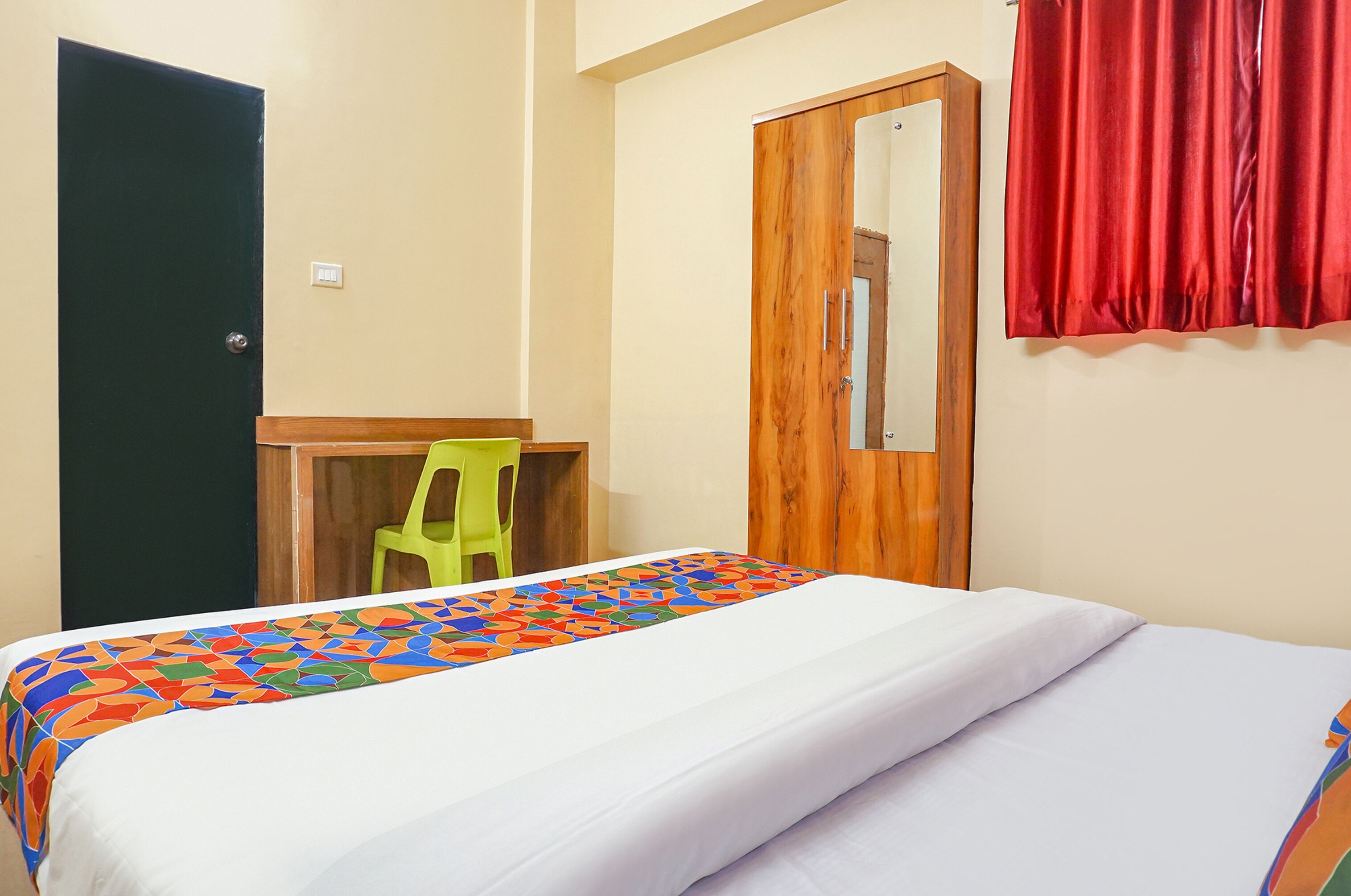 A hotel room with a bed, a desk, a chair, a wardrobe, and a mirror.