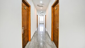 A hallway with wooden doors, a marble floor, and a ceiling with circular light fixtures. - Fabhotel Radiant Blu (Noida)