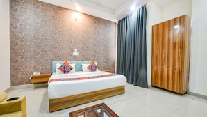 A hotel room with a large bed, wooden headboard, a nightstand, a wooden wardrobe, a small table, and a chair. - Fabhotel Radiant Blu (Noida)