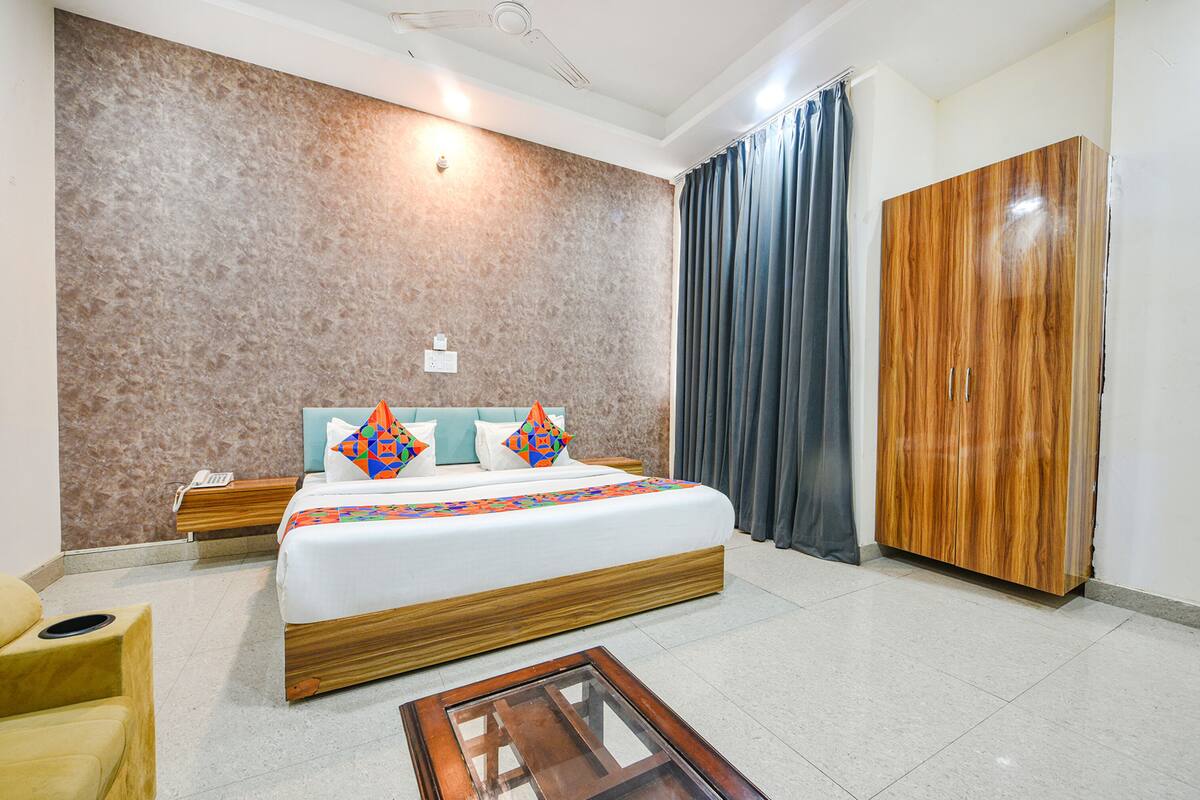 A hotel room with a large bed, wooden headboard, a nightstand, a wooden wardrobe, a small table, and a chair.