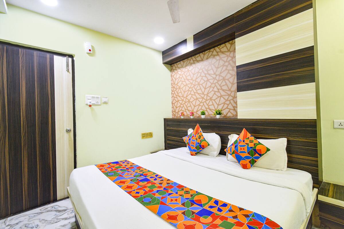 Habitación de hotel con cama, puerta de madera, pared con diseño y un pequeño estante con adornos.