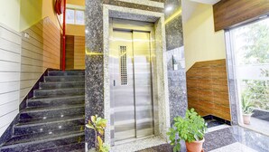 A modern elevator with a metallic finish, a marble staircase, and potted plants.