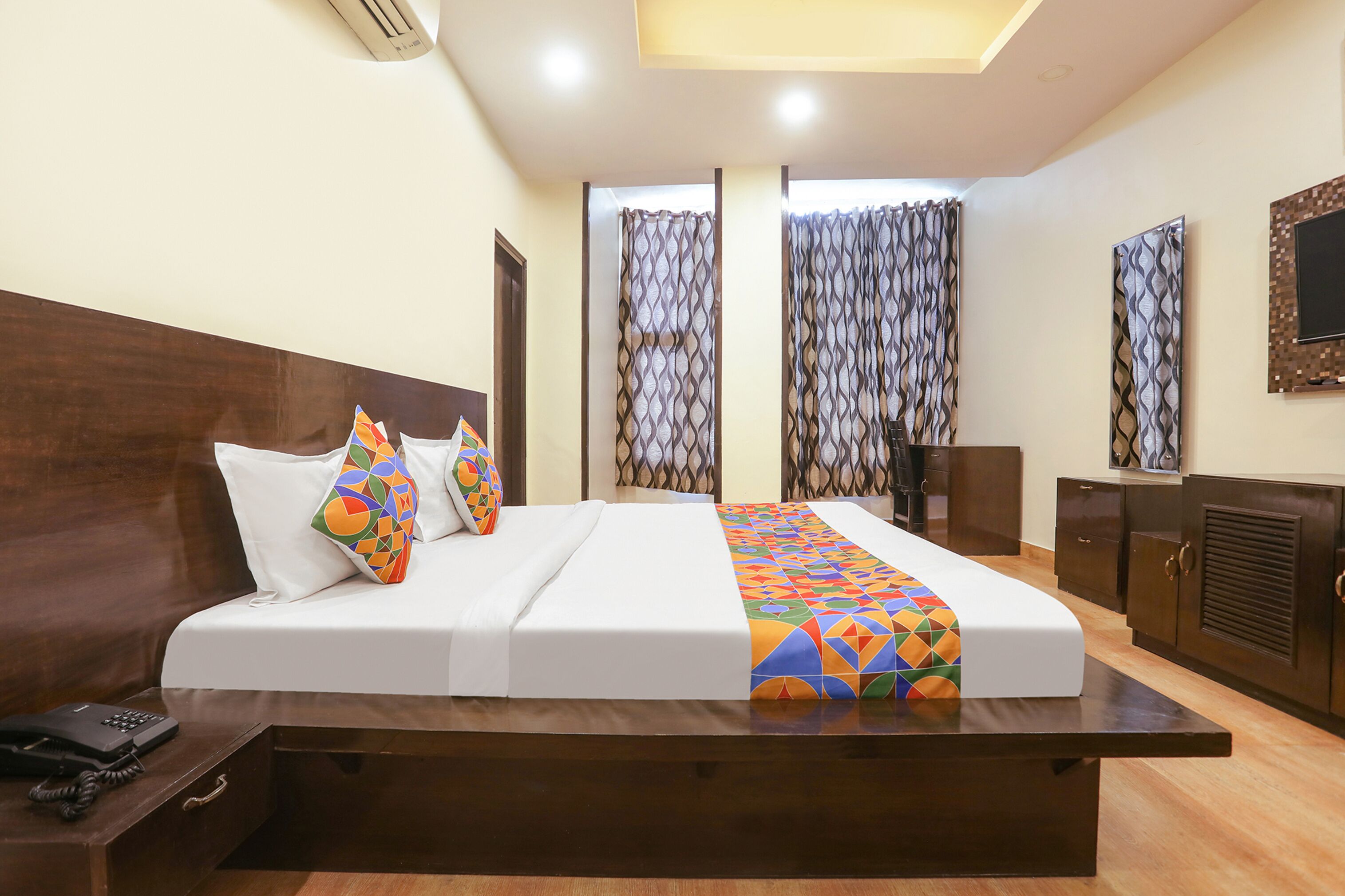 A hotel room with a large bed, a wooden headboard, a bedside table with a phone, and a wardrobe.