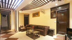 A living room with a brown leather sofa, a glass coffee table with decorative items, and a television on a wooden cabinet. - Fabexpress Rajdeep Palace (New Delhi)