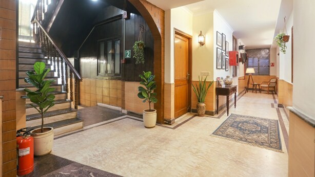 A spacious hallway with a staircase, potted plants, a fire extinguisher, and a dining area with a table and chairs. - Fabexpress Rajdeep Palace (New Delhi)