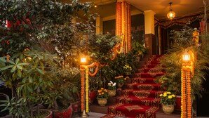 A staircase with red carpet and floral decorations, surrounded by potted plants and traditional lighting fixtures. - Fabexpress Rajdeep Palace (New Delhi)